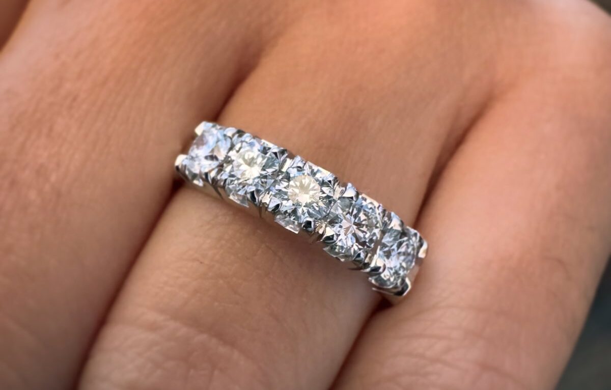 fedina con 5 diamanti in oro bianco 18 carati Fedina di fidanzamento in oro bianco con diamanti rotondi incastonati a griffe, indossata su una mano.