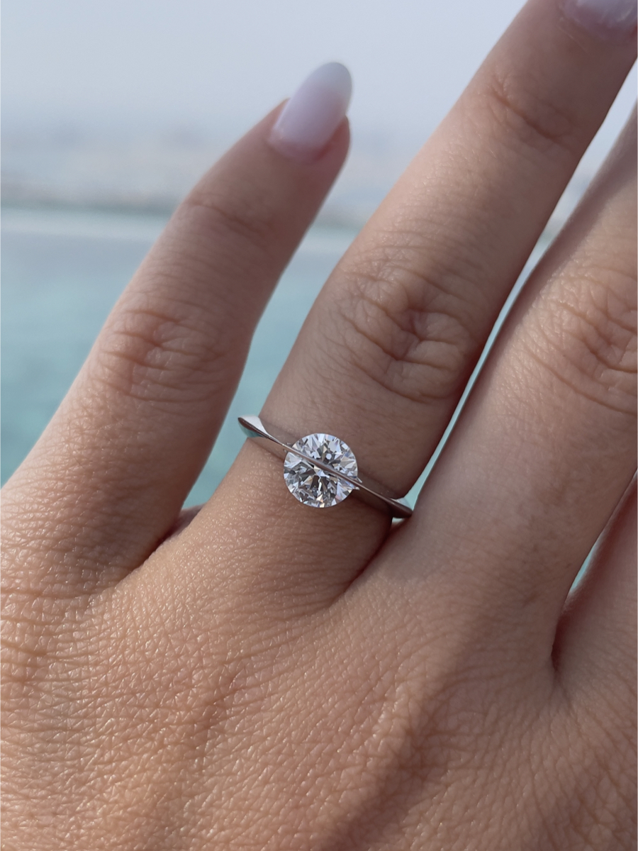 Anello Giroluce indossato su mano femminile, diamante che ruota al centro della montatura minimalista, sfondo marino sfocato