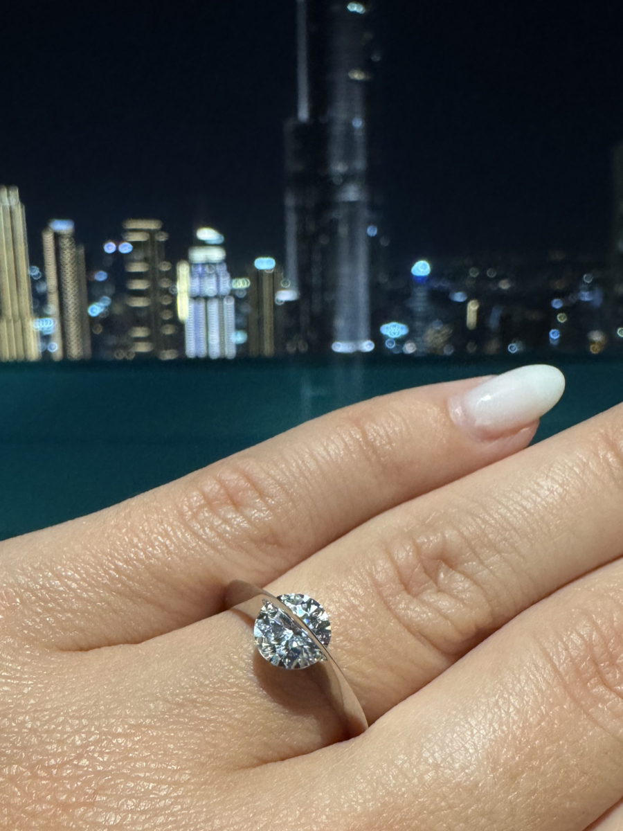 Anello Giroluce indossato con diamante che ruota, mano in primo piano e grattacieli illuminati sullo sfondo