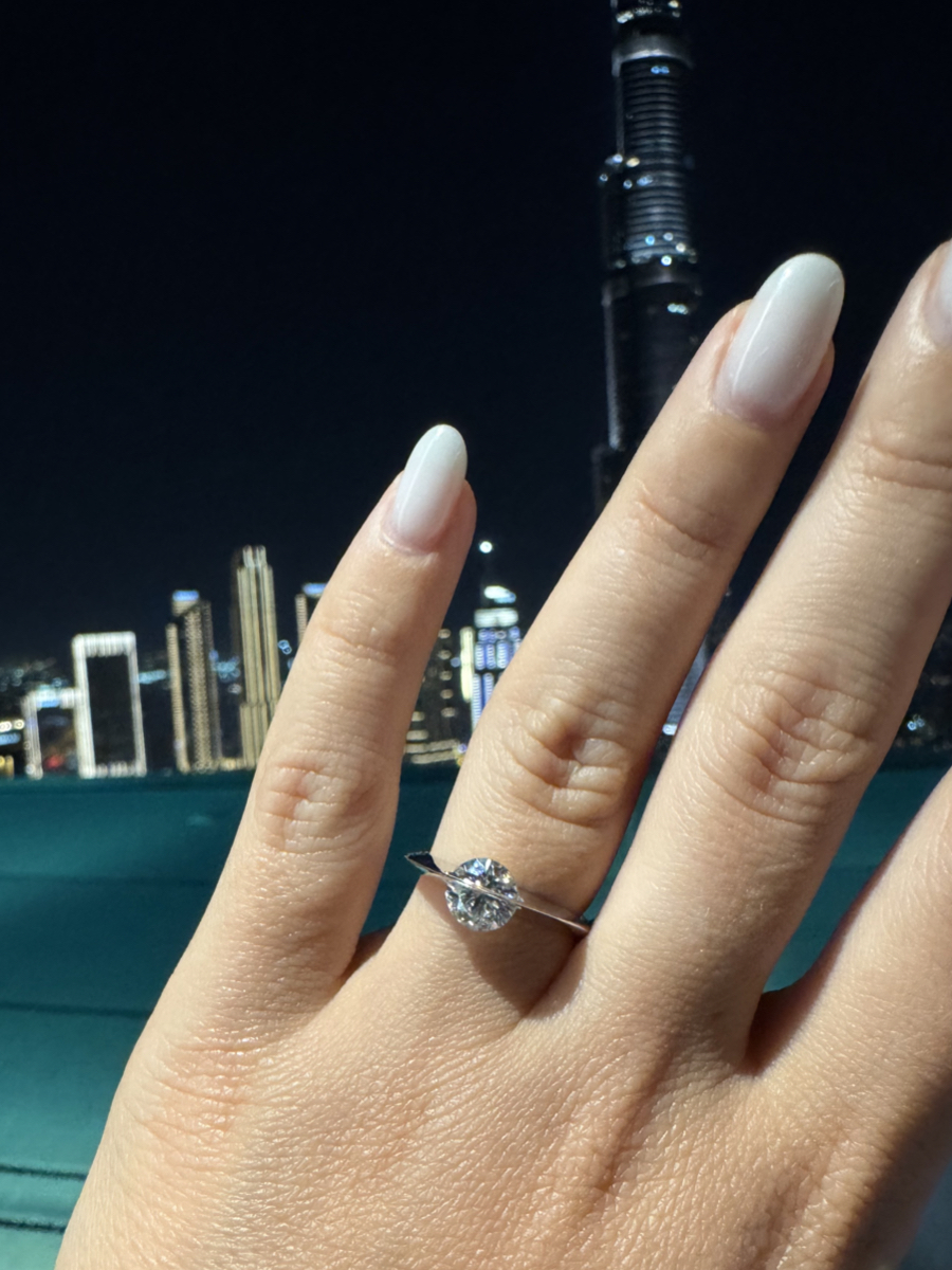 Mano femminile con un anello Giroluce indossato, diamante che ruota su se stesso, sfondo notturno con grattacieli illuminati.