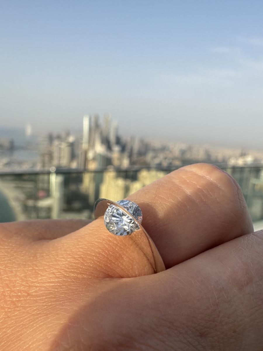 Anello Giroluce indossato con diamante rotante in primo piano, skyline metropolitano sfocato e luce naturale del mattino.
