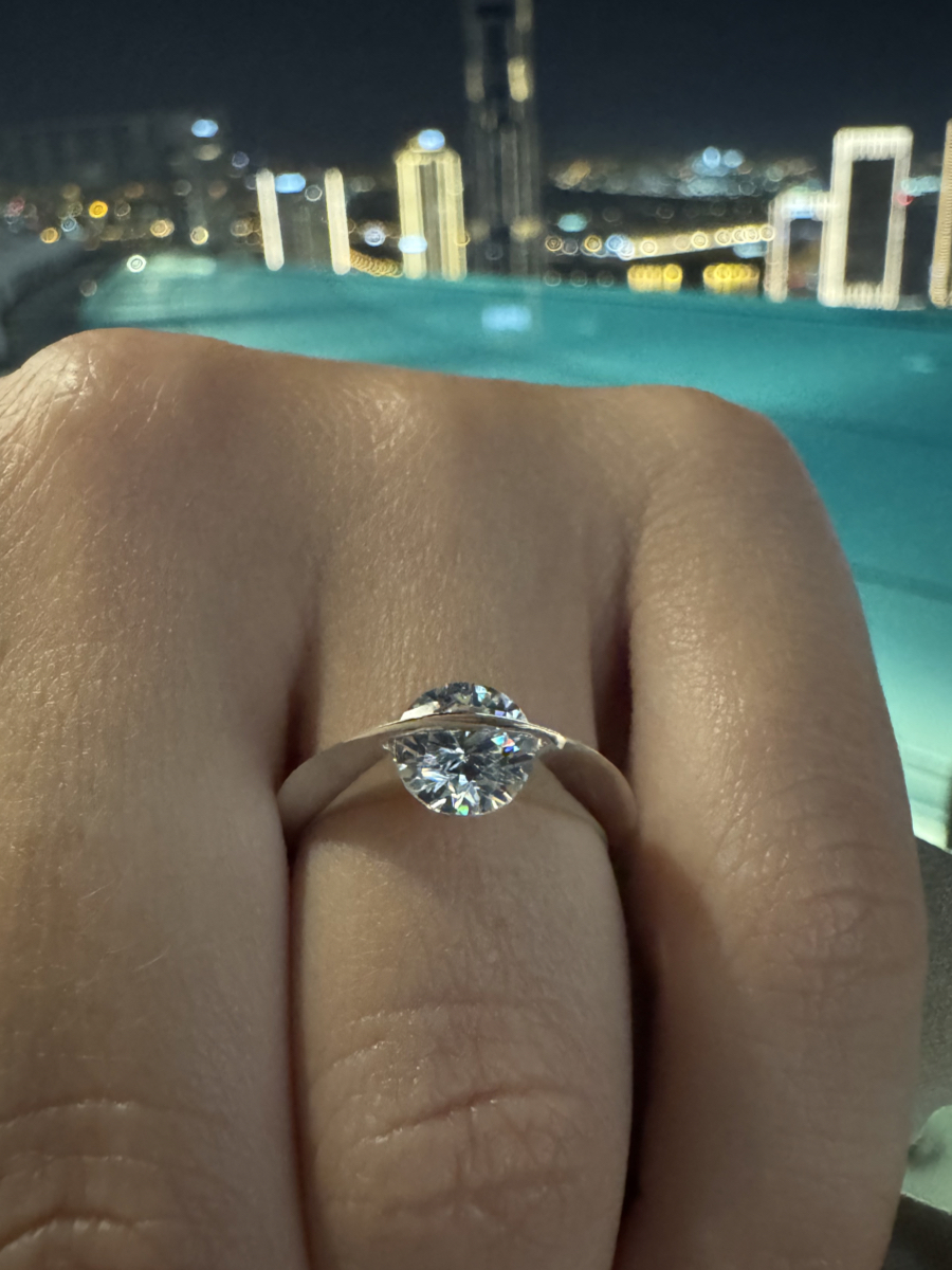 Anello Giroluce indossato, con diamante naturale che ruota su se stesso, montatura in oro minimalista, skyline notturno sullo sfondo.